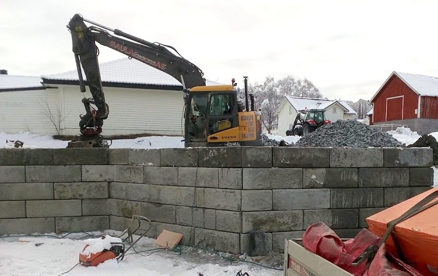 Gravemaskin arbeider over mur av betongblokk